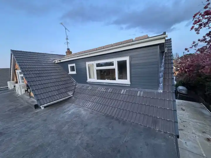Grey clad dormer on a new tiled roof beside a flat roof section